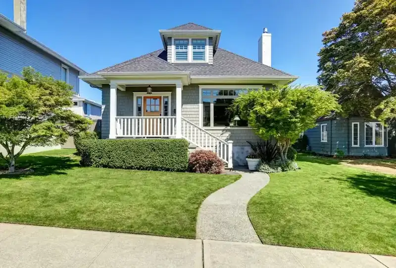 Sunlit two-story house with a green lawn and mature landscaping